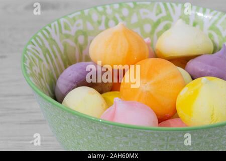 Baisers, verschiedene Farben, in einem grün gemusterten Schüssel Schüssel. Graues Holz Hintergrund Stockfoto