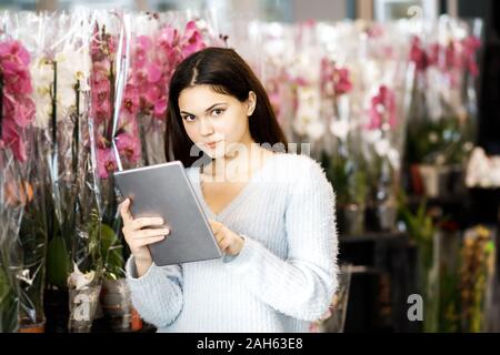 Mädchen gekleidet in einem warmen Pullover hält ein Tablett in den Händen und steht in der Nähe der Orchidee Blumen Stockfoto