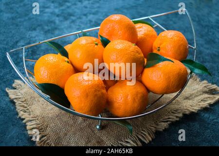 Eine Menge Mandarinen mit Blättern in einer Vase auf einem schwarzen Hintergrund. Stockfoto