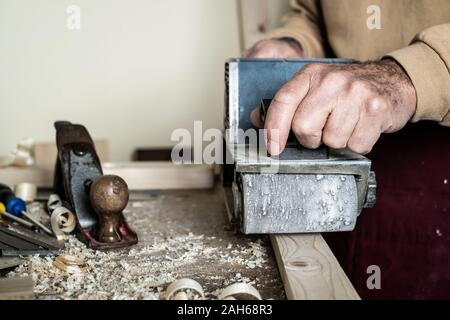 Elektrische Belt Sander, männliche Hand Sander. Werkstückbearbeitung auf hellbraunem Holztisch. Vorderansicht Stockfoto