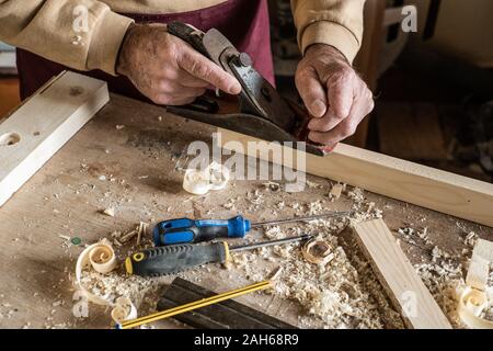 Tischler mann Schaben gewellt Holzresten mit dem Flugzeug Werkzeug und Holzbrett. Stockfoto