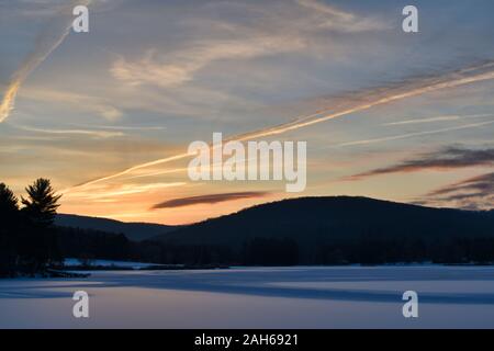 Kalte Sonnenaufgang über Baum bedeckte Hügel und gefrorenes Wasser mit Schnee am Roten Haus See, Allegany State Park, New York Stockfoto