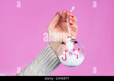 Weibliche Hand ornament Kugel mit Schnee auf rosa Hintergrund im Studio isoliert. Weibliche Hände mit roten Nägeln Polnisch auf die Finger. Weihnachten Konzept Stockfoto