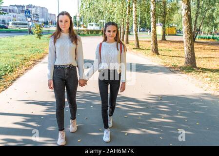 Zwei Mädchen schoolgirls Freunde gehen in der Stadt im Sommer nach homecoming Lektionen. Hinter Rucksäcke, Casual Wear Jeans Pullover. Herbst, Bäume im Hintergrund Stockfoto