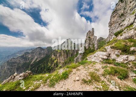 Weitwinkelansicht einer italienischen Alpenlandschaft, mit einem Felsblock und grünem Gras im Vordergrund, und entfernten Monuntains im Hintergrund Stockfoto