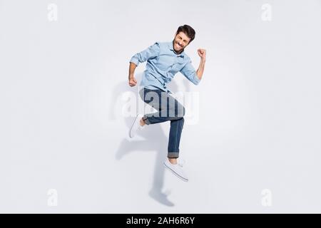 Volle Größe Profil Foto von lustigen indischen Kerl springen hoch Jubeln heben, Fäuste verrückt wettbewerbsfähige Stimmung tragen Casual denim Kleidung isoliert weißer colo Stockfoto