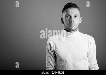 Junger Mann tragen weiße rollkragen pullover gegen grauer Hintergrund Stockfoto