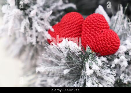 Weihnachten Herz, Tag Valentinstag Karte, zwei Rote gestrickt, Symbole der Liebe im Schnee auf tannenzweigen. Hintergrund für romantische Ereignis, neues Jahr Stockfoto