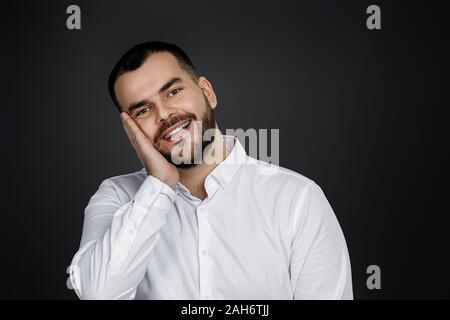 Close-up Portrait von lächelnden aussehenden bärtigen Mann an der Kamera schaut auf schwarzem Hintergrund Stockfoto