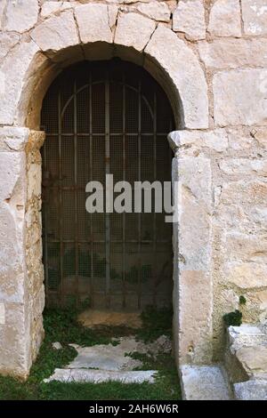 Eingang mit einem Bogen in den steinernen Stadtmauer, geschlossen mit Eisenstangen, mit Gras bewachsen. Stockfoto