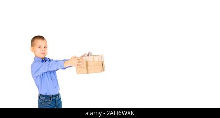 Ein Junge in einem lila Hemd mit einem Geschenk aus dem craft-Papier in seinen ausgestreckten Händen auf einem weißen Hintergrund, isoliert auf Weiss. Urlaub Konzept. Banner. Stockfoto