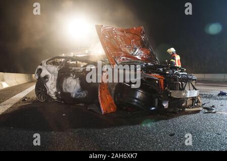 Ehningen, Deutschland. 26 Dez, 2019. Ein Feuerwehrmann steht vor einem Ausgebrannten Autowrack auf der Autobahn 81. Zwei 38 und 24 Jahre alten Männer von ihren brennenden Auto nach einem Unfall auf der Autobahn 81 im Kreis Böblingen, schwer verletzt gerettet wurden. (Dpa' Fahrzeug in Brand auf der A81: Verletzte aus der Passagiere gerettet) Credit: Dettenmeyer/SDMG/dpa/Alamy leben Nachrichten Stockfoto