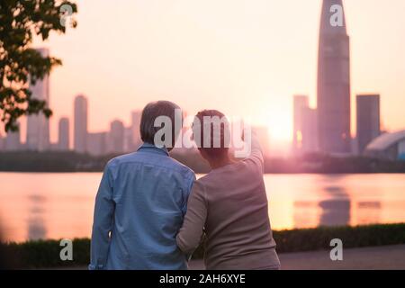 Ansicht der Rückseite des Älteren asiatischen Paar suchen bei Sonnenaufgang und die Skyline der Stadt vom Fluss Stockfoto