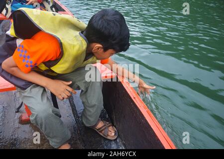 Ein junger Mann, Rettungsweste sitzen auf einem hölzernen Boot Gefühl das Wasser wie es segelt in Dawki Fluss shillong in Meghalaya. Stockfoto