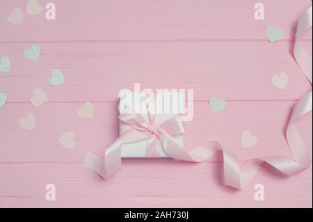 Geschenkbox mit Schleife und Konfetti in Form von Herzen auf rosa Holz- Hintergrund mit Platz für Ihren Text. Mock up am Valentinstag, Muttertag oder Stockfoto