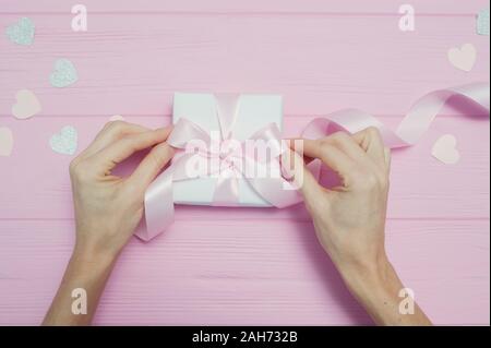 Valentinstag Liebe Konzept der Schönen womans Hände halten Geschenkbox Handwerk Papier und Herz Konfetti auf rosa Hintergrund. nach oben Blick flach mit Platz für Stockfoto