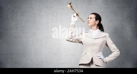 Schöne Frau spielen Trompete Messing. Junge businesslady in weissem Anzug und Handschuhe mit Musik Instrument posiert auf grauen Hintergrund. Musi Stockfoto