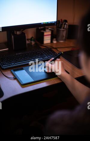 Eine Frau mit Grafik Tablett mit Stift und arbeitet sie an ihrem Schreibtisch im trüben Licht des Monitors Stockfoto