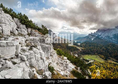 Weitwinkelansicht einer typischen alpinen Landschaft, mit einem felsigen Hang auf der linken Seite und einem Tal von Pinien auf der rechten Seite, unter geschwollenen Wolken bedeckt Stockfoto