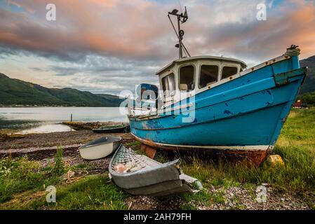 Sonnenaufgang auf einem abgelegenen schottischen See mit einem blauen Fischer Boot im Vordergrund und ferne Hügel im Hintergrund Stockfoto