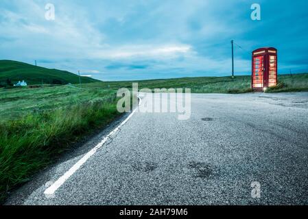 Auf einer ländlichen schottischen Straße in der Nacht liegt eine einsame britische rote Telefonzelle an der Bordwand Stockfoto