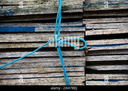 Nahaufnahme eines Stapels verwitterter Holzbretter gehalten Zusammen durch eine blaue Nylonrobe mit einem Bogenknoten Stockfoto