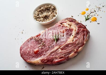 Teil von rohem Rindfleisch ohne Knochen ribeye Steak Marmor mit Fett, gewürzt mit Kräutern und Gewürzen bereit zum Grillen auf einem grauen studio Hintergrund Stockfoto