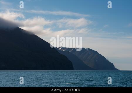 Die ikonische isländische Seenlandschaft mit einer Reihe von Bergen, die unter einem blauen Himmel mit geschwollenen Wolken zum Meer abfallen Stockfoto