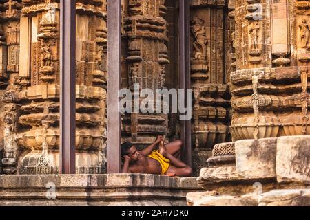 Bhubaneshwar, Orissa, Indien - Februar 2018: Außenfassade eines antiken Tempels mit Schnitzereien von Hindu-Götter und Göttinnen an den Wänden. Ein Priester Stockfoto