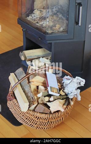 Retro Weidenkorb mit Brennholz und Matches steht vor einem Kamin Stockfoto