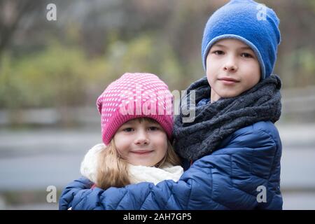 Zwei Kinder, Junge und Mädchen umarmten einander im Freien tragen warme Kleidung in der kalten Herbst oder Winter Wetter. Stockfoto