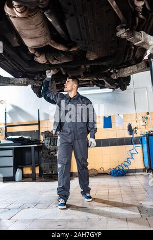 Junge Mechaniker Prüfung von unten angehoben Auto in Werkstatt Stockfoto