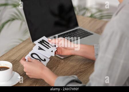 7/8-Ansicht von Astrologen halten Karten mit Sternzeichen neben Laptop und Kaffee auf Tisch Stockfoto