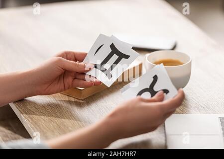 7/8-Ansicht von Astrologen halten Karten mit Sternzeichen neben Kaffee und Buch auf Tabelle Stockfoto