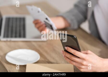 Selektiver Fokus der Astrologe holding Smartphone und Karten mit Sternzeichen durch Laptop am Tisch, 7/8-Ansicht Stockfoto