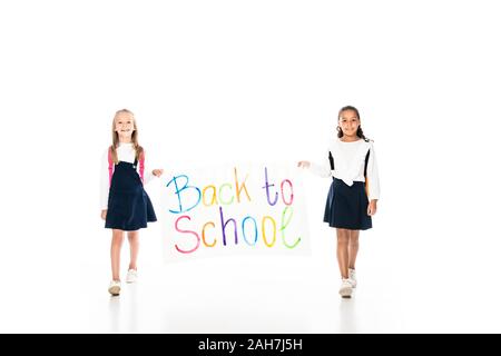 Volle Länge aussicht auf zwei multikulturelle Schülerinnen holding Plakette mit Inschrift zurück zur Schule beim Gehen auf weißem Hintergrund Stockfoto