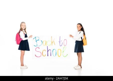 Volle Länge aussicht auf zwei multikulturelle Schülerinnen mit Rucksäcken holding Plakat mit zurück in die Schule Beschriftung auf weißem Hintergrund Stockfoto