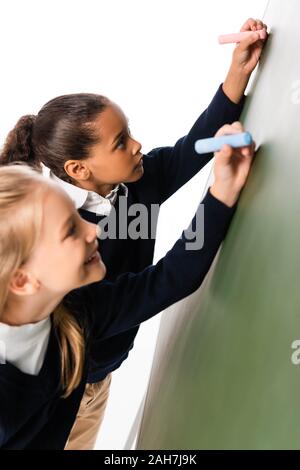 Zwei adorable multikulturelle Schülerinnen schreiben auf grüner Tafel Stockfoto