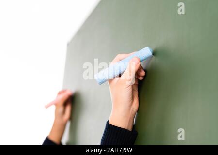 Parftial aussicht auf zwei multikulturelle Schülerinnen schreiben auf der Schiefertafel isoliert auf weißem Stockfoto