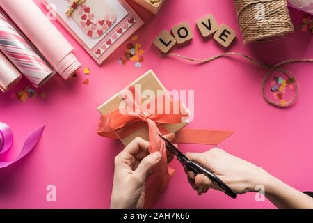 7/8-Ansicht von Frau schneiden ribbon Während Valentines Geschenk auf rosa Hintergrund Stockfoto