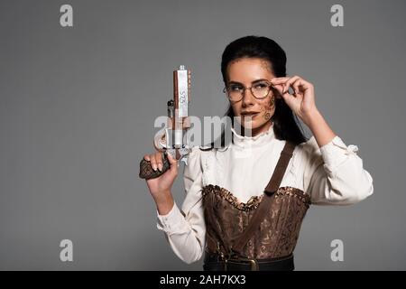 Nachdenklich steampunk Frau mit Vintage Pistole und berühren Gläser isoliert auf Grau Stockfoto