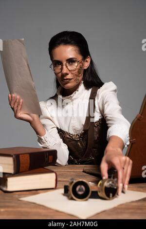 Steampunk Frau mit Dokument und Brille am Arbeitsplatz isoliert auf Grau Stockfoto