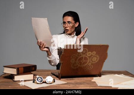 Steampunk Frau am Tisch sitzend mit Vintage Laptop und Bücher und Dokumente isoliert auf Grau besorgt Stockfoto