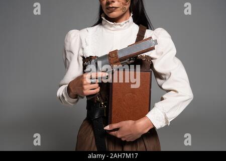 7/8-Ansicht von steampunk Frau mit Buch und vintage Pistole auf Grau Stockfoto