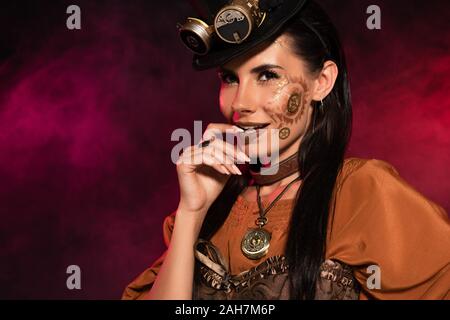 Attraktive steampunk Frau lächelnd und beißen Finger in rosa Rauch Stockfoto