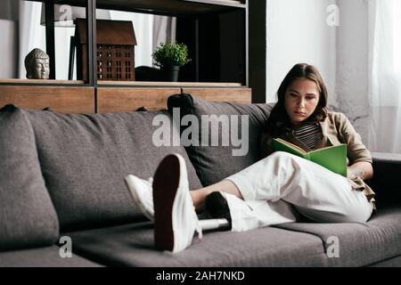 Selektiver Fokus der Frau mit Prothese lesen Buch auf der Couch im Wohnzimmer. Stockfoto