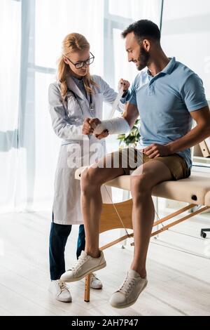 Attraktive Orthopäde, Verband auf verletzte Hand von glücklichen Mann Stockfoto