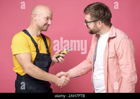 Zufrieden und dankbar Client macht einen Handshake Geste mit einem Arbeiter, der einen guten Job gemacht hat. Stockfoto