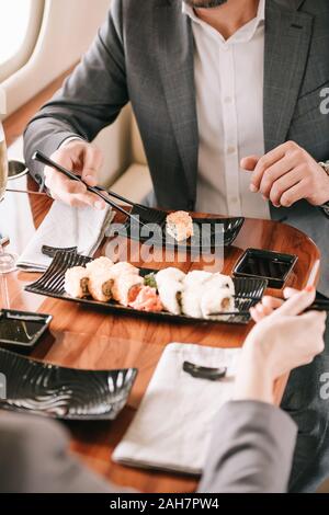 Der Geschäftsmann und Geschäftsfrau holding Stäbchen in der Nähe von Sushi in Private Jet 7/8 Stockfoto