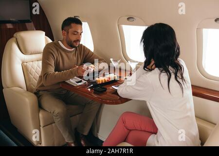Von hinten Sitzende Frau mit der Mann in der Nähe von Sushi und Martini Gläser in Private Jet Stockfoto